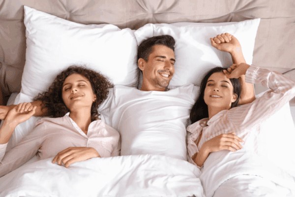 mężczyzna w łóżku z dwiema kobietami poligamia czyli m.in stosunki seksualne z wieloma kobietami