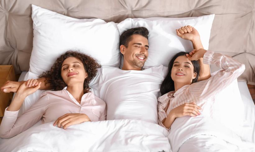mężczyzna w łóżku z dwiema kobietami poligamia czyli m.in stosunki seksualne z wieloma kobietami