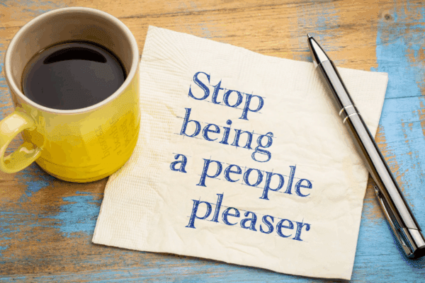 people pleaser napisane na kartce a obok stoi kubek z kawą