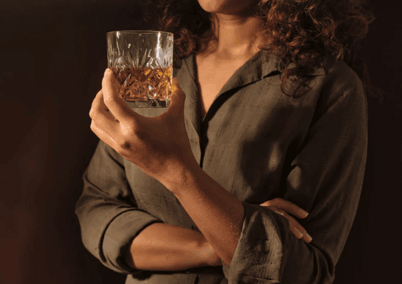 uzależnienie od alkoholu; Na zdjęciu widać osobę trzymającą szklankę z alkoholem, co może symbolicznie nawiązywać do picia alkoholu oraz tematów związanych z uzależnieniem. Tego typu obraz bywa wykorzystywany w kontekstach omawiających rozwiązywanie problemów wynikających z nadużywania substancji, wpływ alkoholu na ich życie, a także konsekwencje zdrowotne, takie jak marskość wątroby czy inne formy choroby związanej z nałogiem. W materiałach edukacyjnych podobne ujęcia mogą podkreślać, jak negatywne emocje, samotność i problemy z przystosowaniem prowadzą czasem do prób sięgania po alkohol oraz jak rozwija się choroba alkoholowa i nadmierne picie.