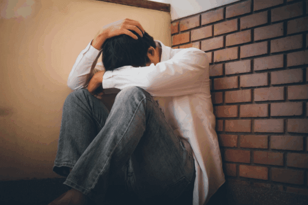 zaburzenia depresyjno-lękowe, mężczyzna opiera się o ścianę, ma twarz w dłoniach