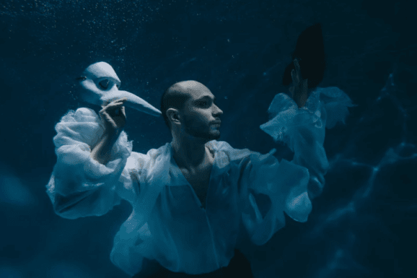 urojenia; mężczyzna, który trzyma dwie maski. Scena ta może symbolicznie przedstawiać urojenia paranoiczne, w których pojawiają się nieprawidłowe przekonania oderwane od realności. Postać jakby balansuje między dwiema tożsamościami, co można odnieść do życia pacjenta z zaburzeniami psychicznymi, w którym występują złożone zależności emocjonalne i psychiczne. Atmosfera obrazu mogłaby też sugerować wpływ alkoholu, który często potęguje stany urojeniowe w kontekście psychiatrii.