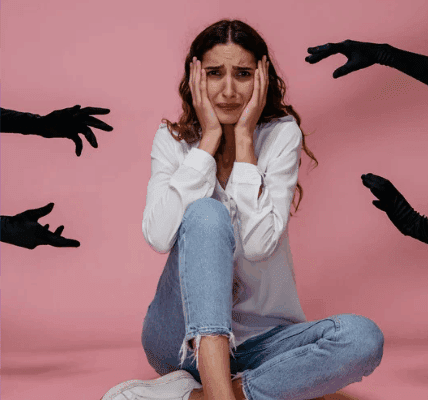 osobowość paranoiczna, Na zdjęciu widać młodą kobietę siedzącą na podłodze, wyglądającą na przestraszoną i przytłoczoną, podczas gdy z różnych stron zbliżają się do niej czarne, wyciągnięte dłonie. Scena może symbolicznie nawiązywać do zaburzeń psychicznych i presji, która wpływa na funkcjonowanie człowieka. Układ dłoni może metaforycznie przypominać cechy osobowości paranoicznej, takie jak poczucie zagrożenia czy nadmierna czujność, które utrudniają relacje interpersonalne oraz dostosowanie do norm społecznych.  W takim ujęciu obraz może też kojarzyć się z problemami pojawiającymi się w życiu prywatnym, np. nieufnością wobec wierności partnera, czy lękami, które mogą nasilać substancje psychoaktywne, wywołując podobne objawy napięcia i niepokoju. Jednocześnie całość może sugerować potrzebę wsparcia, jaką daje terapia, pomagająca uporządkować emocje i doświadczenia.