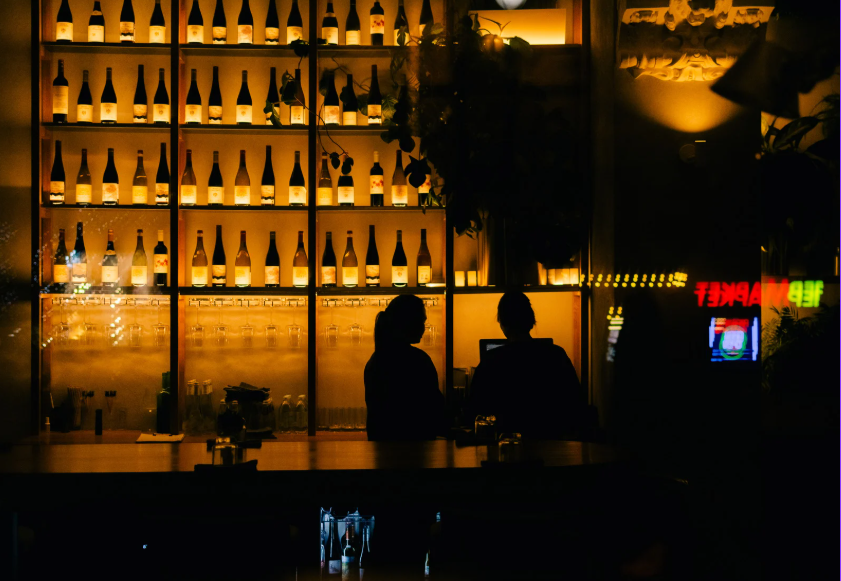 DDA - dorosłe dzieci alkoholików; syndrom DDA; Na zdjęciu widać ciemne wnętrze baru, co może symbolicznie nawiązywać do historii osób wychowanych przy problemie alkoholowym. Atmosfera miejsca przywołuje skojarzenia z tym, jak rozwija się syndrom DDA u dorosłych dzieci alkoholików. Cień postaci może odzwierciedlać niskie poczucie własnej wartości i trudność w zauważaniu własnych potrzeb. Taka sceneria podkreśla też, jak syndrom DDA wpływa na relacje partnerskie. Tło baru, pełne bodźców, można odczytać jako metaforę obciążenia psychicznego, jakie niesie zaburzone zdrowie psychiczne w dorosłości. Dodatkowo taka barowa sceneria może symbolicznie przywoływać doświadczenia osób dorastających w rodzinie alkoholowej, gdzie choroba alkoholowa jednego z domowników kształtowała atmosferę domu. W tle można wyobrazić sobie także poczucie winy i nawet fizyczne objawy napięcia. Rozwój syndromu DDA może wynikać z długotrwałego funkcjonowania w rodzinie alkoholowej i kumulowania trudnych emocji.