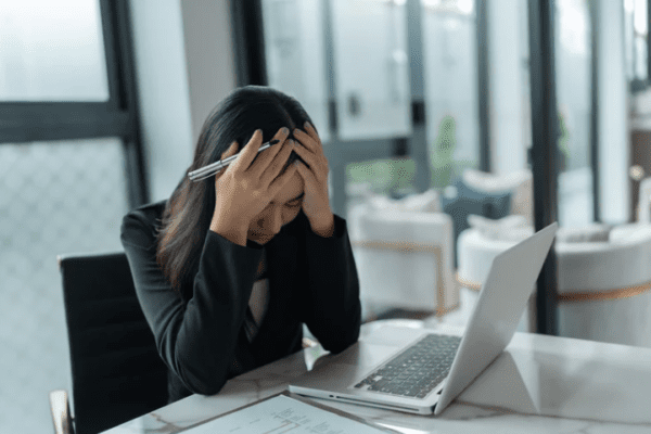 uzależnienie od stresu, kobieta siedząca w pracy trzymająca się za głowę