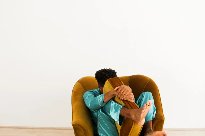 lęk a strach; Na zdjęciu widać osobę skuloną w fotelu, obejmującą nogi, co może symbolizować zaburzenia psychiczne oraz silne uczucia przytłoczenia. Taka postawa bywa kojarzona z lękiem uogólnionym, w którym lękiem i lęki pojawiają się nawet bez realnego zagrożenia, choć są przeżywane jako realnym zagrożeniem. Obraz sugeruje napięcie, poczucie zagrożenia oraz różne dolegliwości emocjonalne; można odnieść wrażenie, że osoba cierpi i zmaga się ze stanami podobnymi do depresji.