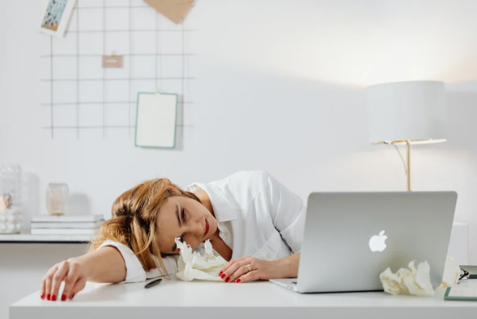 zmęczenie psychiczne; kobieta leży na biurku przed laptopem, wydaje się być bardzo zmęczona
