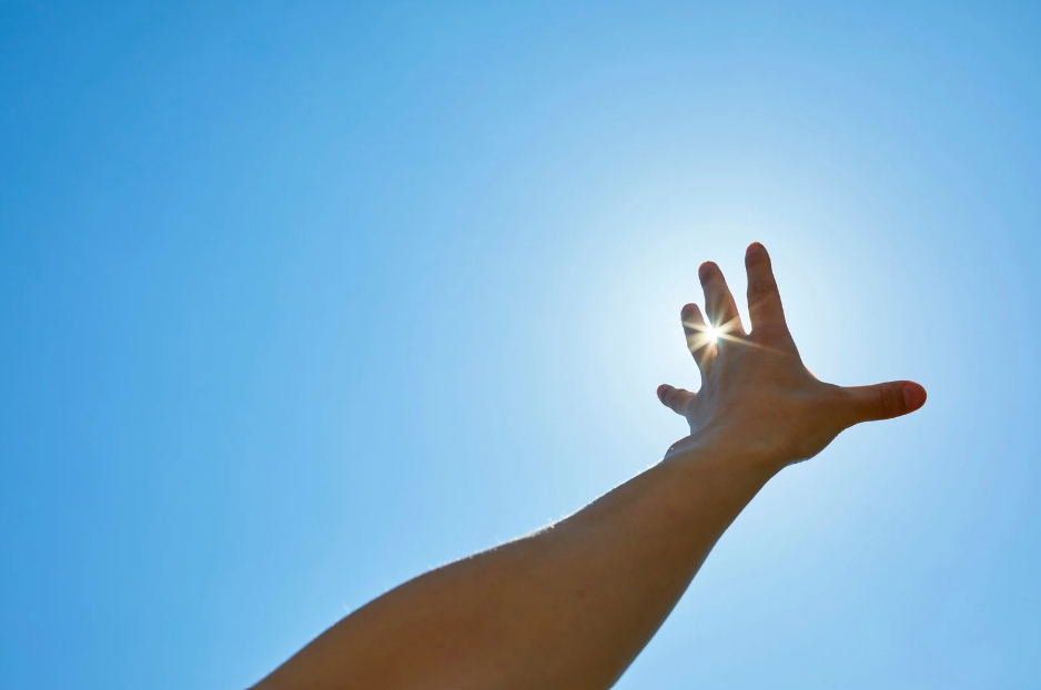 marzenia; zdjęcie przedstawia wyciągniętą rękę w stronę słońca, co może symbolizować dążenie do realizacji marzeń i własnych fantazji