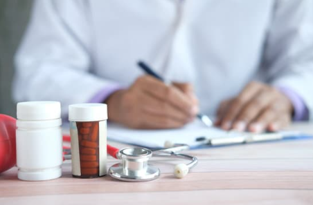 jak działają psychotropy - w tyle zdjęcia lekarz wypisujący receptę, a przed nim na biurku znajduje się kilka leków