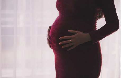nerwica poporodowa objawy - zdjęcie przedstawia brzuch ciążowy kobiety ubranej w dopasowaną czerwoną sukienkę