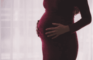 nerwica poporodowa objawy - zdjęcie przedstawia brzuch ciążowy kobiety ubranej w dopasowaną czerwoną sukienkę