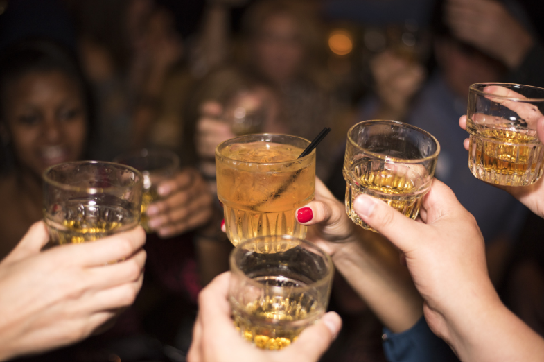 ataki paniki po alkoholu - na zdjęciu młodzi ludzie wznoszą toast trzymając w rękach szklanki z alkoholem
